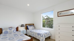 A bedroom with two single beds, a nightstand, a dresser, and a window with a view of greenery.