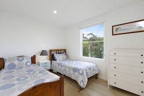 Une chambre avec deux lits simples, une table de chevet, une commode et une fenêtre donnant sur un paysage verdoyant.