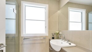 A modern bathroom with a large mirror, a sink, and a glass shower enclosure. - Godalming (Lorne)