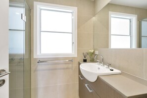 A modern bathroom with a large mirror, a sink, and a glass shower enclosure. - Godalming (Lorne)