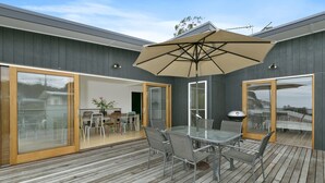 An outdoor patio with a glass table and chairs, a large umbrella, and a grill. - Godalming (Lorne)