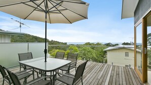 A wooden deck with a table and chairs, an umbrella, and a view of the sea. - Godalming (Lorne)