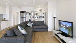 A modern living room with a grey sectional sofa, a flat-screen TV, and a white entertainment unit.