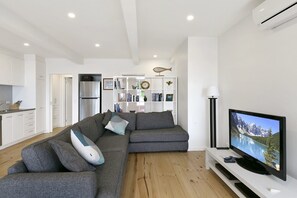 Un salon moderne avec un canapé d’angle gris, un téléviseur à écran plat et un meuble de rangement blanc.