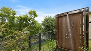 A wooden outdoor shower enclosure with a metal hose and a wooden fence surrounding it.