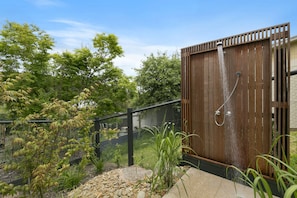 Une cabine de douche extérieure en bois, dotée d’un tuyau en métal et entourée d’une clôture en bois.