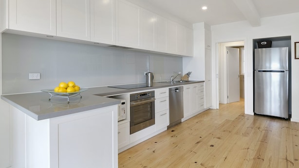 A modern kitchen with white cabinets, stainless steel appliances, and a wooden floor.