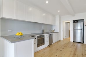 A modern kitchen with white cabinets, stainless steel appliances, and a wooden floor.