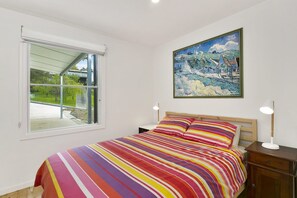 A bedroom with a large window, a bed with striped bedding, a painting on the wall, and bedside lamps.