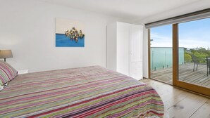 A bedroom with a bed, a painting, a wardrobe, and a balcony with a view. - Godalming (Lorne)