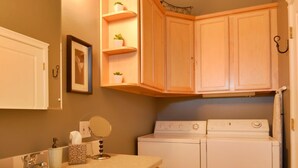 Una cocina compacta con armarios de madera, lavadora y secadora integradas, un lavamanos y un espejo.