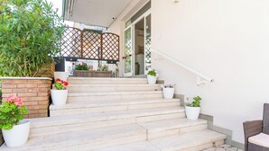 Un conjunto de escalones de piedra que conducen a una puerta, rodeados de plantas en macetas y una silla de mimbre.