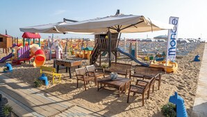 Zona de playa con un parque infantil, asientos y sombrillas.