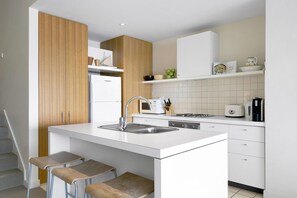 A modern kitchen with a central island, white cabinetry, and a wooden accent wall. - Apartment 25 Kalimna (Lorne)
