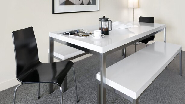 A modern hotel room with a white table, black chairs, a coffee maker, a framed picture, and a lamp. - Apartment 25 Kalimna (Lorne)