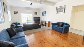 A living room with a large sofa, a smaller sofa, a TV, and a bookshelf.