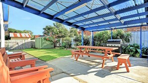 Un patio techado con mesas de picnic y una parrilla.