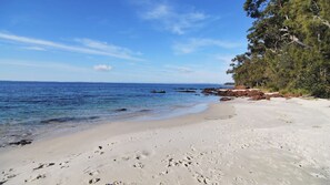 Ein sandiger Strand mit deutlichen Fußspuren, ruhigem Meer und blauem Himmel.