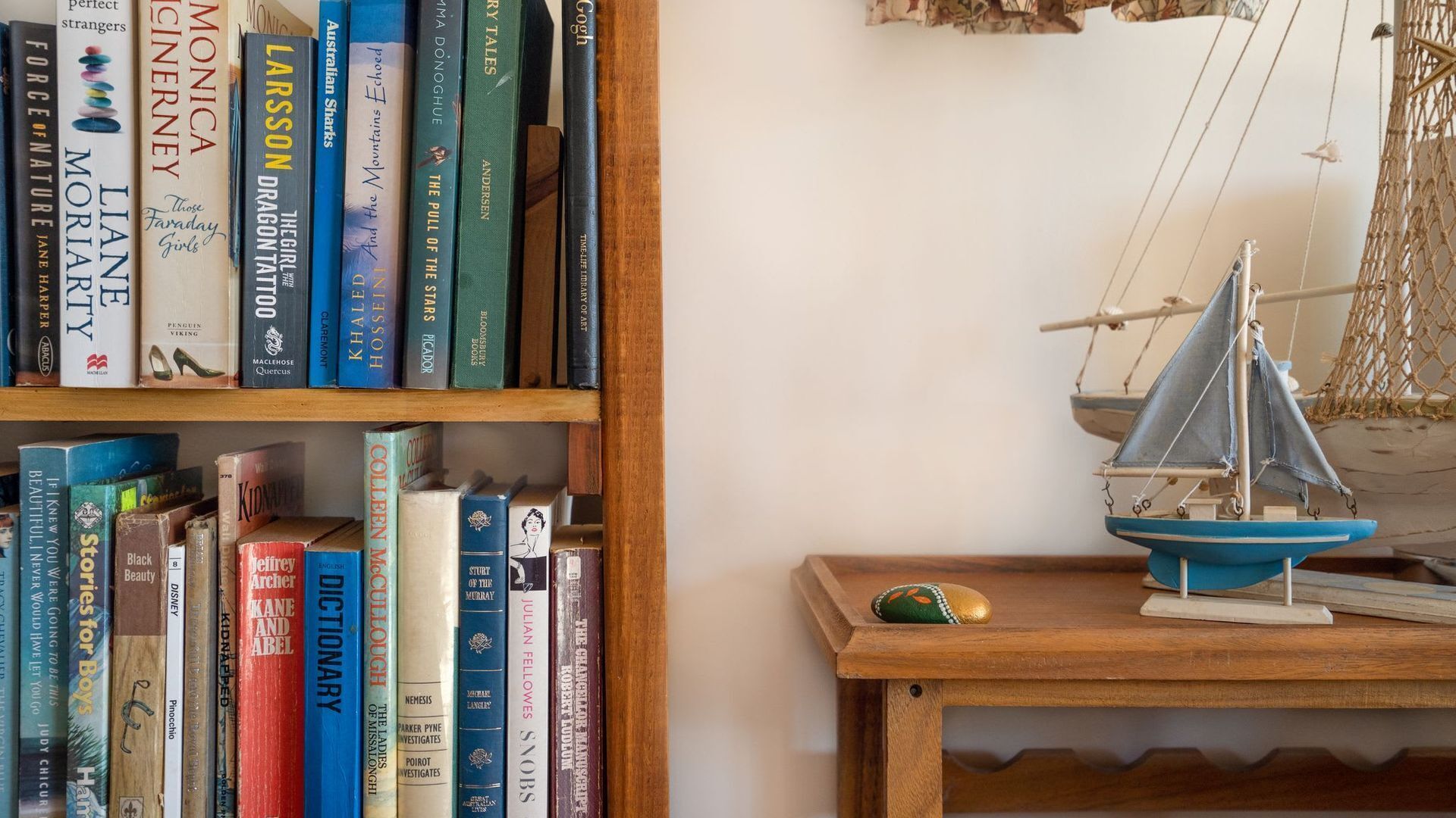 A bookshelf with various books and a small model sailboat on a wooden table.