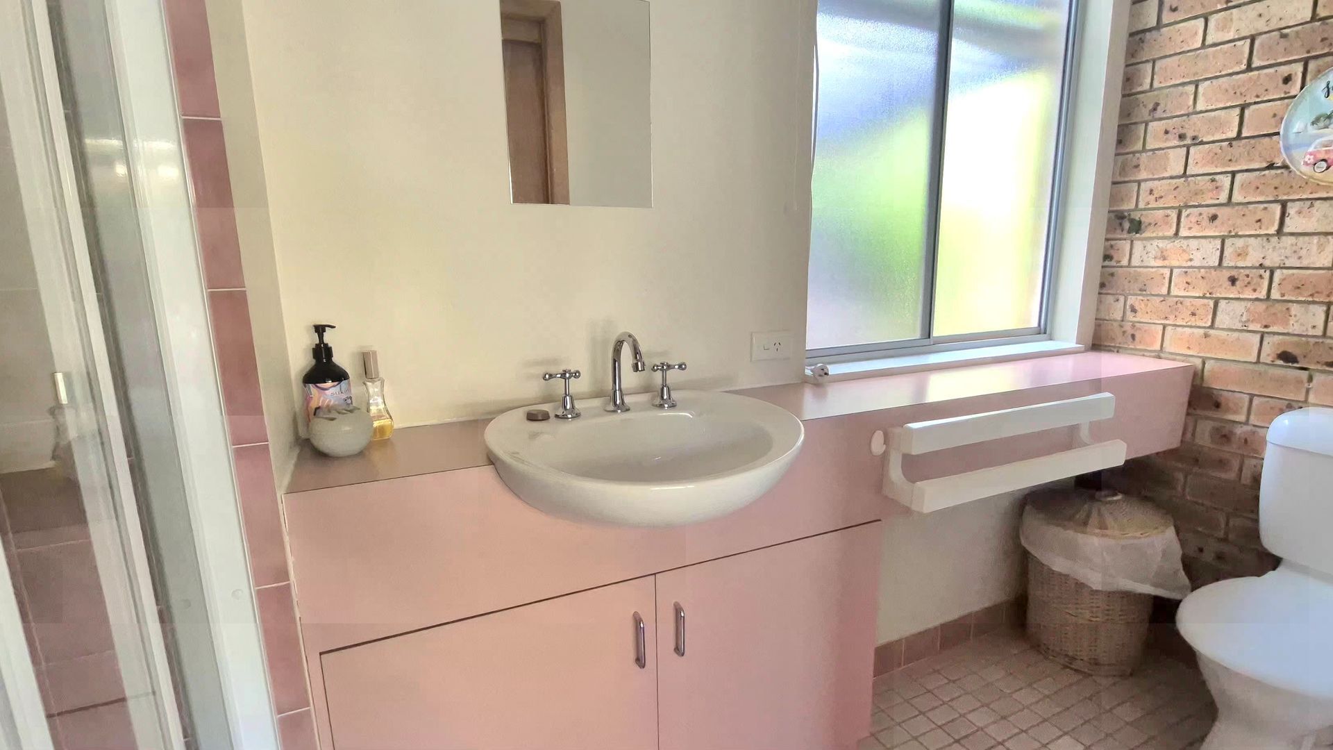 A bathroom with a white sink, a mirror, and a window.