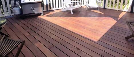 A wooden deck with a grill, outdoor seating, and a view of the surrounding area.