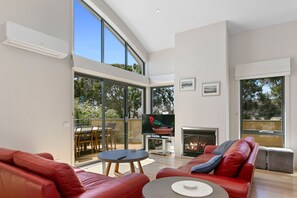 A spacious living room with a fireplace, red leather sofa, and a large sliding glass door leading to an outdoor area. - Cape Vista 1 (Apollo Bay)