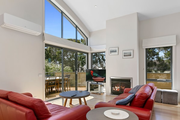 A spacious living room with a fireplace, red leather sofa, and a large sliding glass door leading to an outdoor area.
