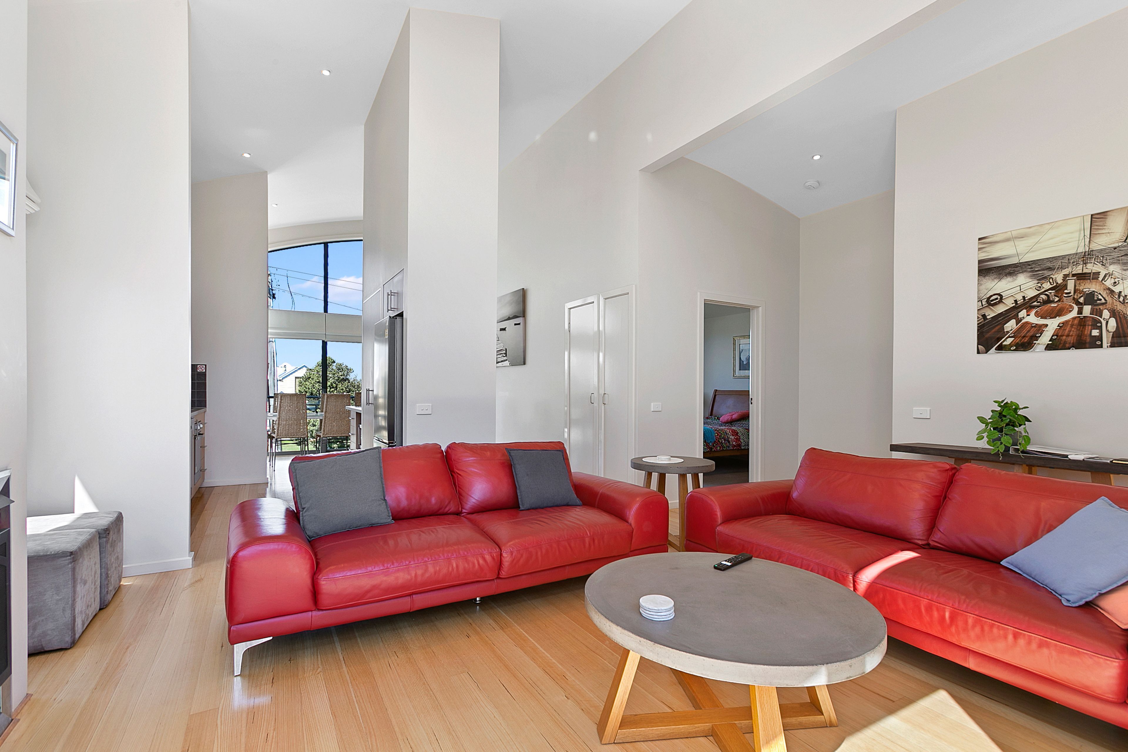 A spacious living room with a red leather sofa set, a round coffee table, and a view of the outdoors through large windows.