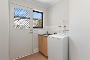 A compact kitchen with a washing machine, a sink, and a window with a view of buildings.