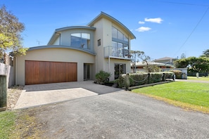 A modern two-story house with a curved facade, a wooden garage door, and a small front yard with a gravel driveway.