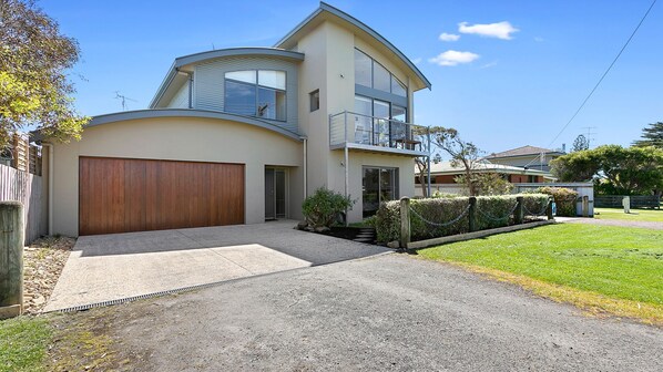 A modern two-story house with a curved roof, a large garage, and a well-maintained lawn.