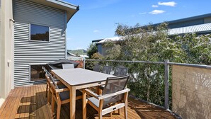 Une terrasse extérieure avec une table et des chaises, donnant sur une maison, et bordée d’une clôture.