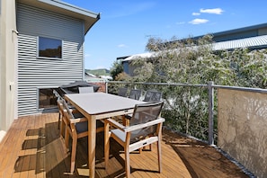 En udendørs terrasse med et bord og stole, udsigt til et hus og et hegn.