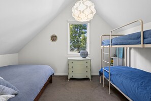 Ein Schlafzimmer mit Etagenbetten, einem Schminktisch, einem Fenster mit Blick auf Bäume und einer Zierleuchte.