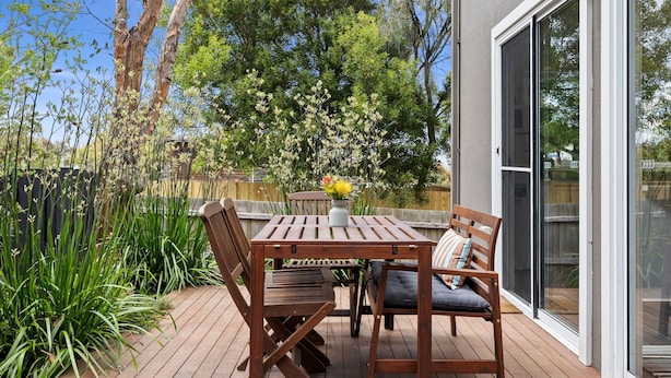 An outdoor patio with a wooden table and chairs, a bench, and a potted plant.