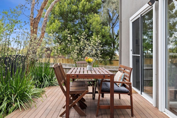 An outdoor patio with a wooden table and chairs, a bench, and a potted plant.