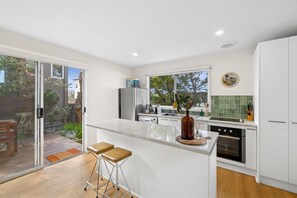 A modern kitchen with a large island, a dining area with a wooden table and bar stools, and a sliding glass door leading to a patio.