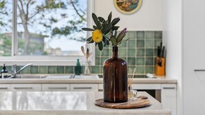 En brun vase med en gul blomst og grønne blade på en køkkenbordplade.