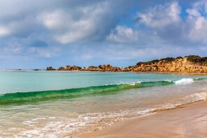 A beach with clear turquoise water, a sandy shore, and rocky cliffs in the background.
