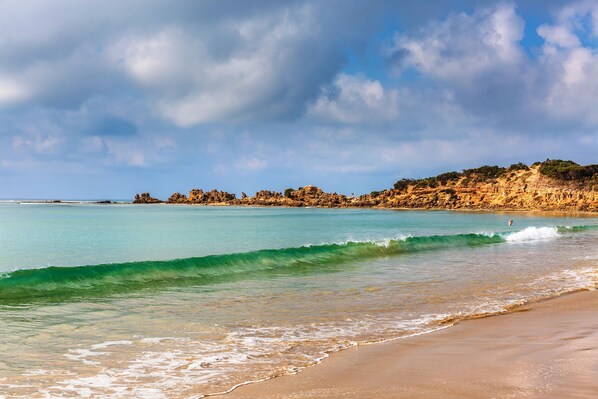 A beach with clear turquoise water, a sandy shore, and rocky cliffs in the background.