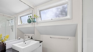 A modern bathroom with a white sink, mirror, and a window above the sink.