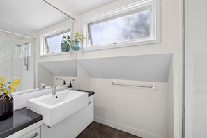 A modern bathroom with a white sink, mirror, and a window above the sink.