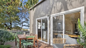 A deck with a table and chairs, a wicker sofa, and a glass door leading to an interior space.