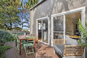 A deck with a table and chairs, a wicker sofa, and a glass door leading to an interior space.