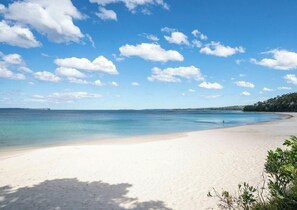 En strand med kristallklart blått vatten, vit sand och några få, utspridda moln.