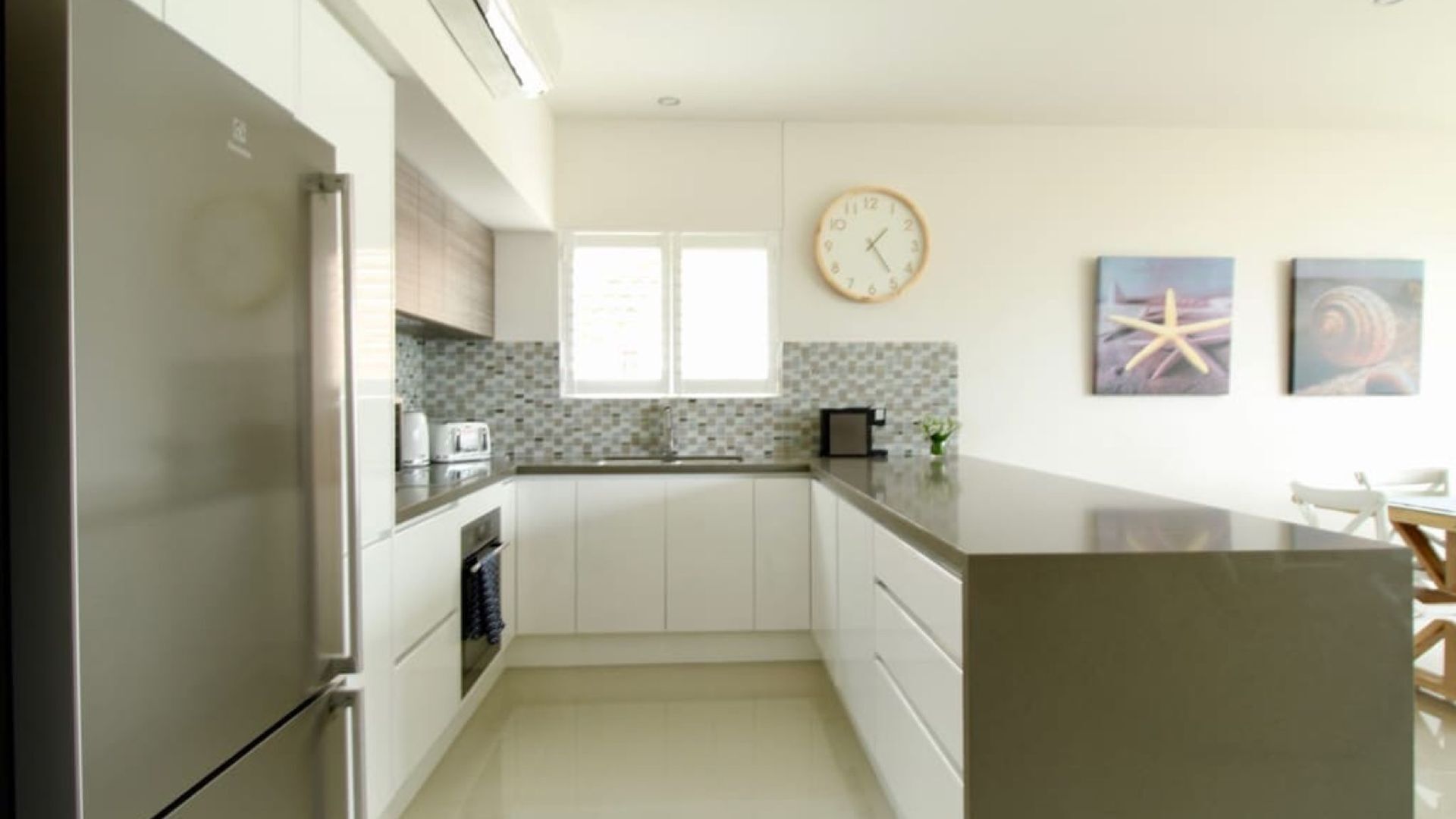 A modern kitchen with white cabinets, a stainless steel refrigerator, a microwave, and a large island.