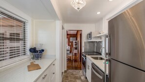 A compact kitchen with a stainless steel refrigerator, a microwave, and a sink. There is a window with blinds, a countertop with a cutting board, and a basket with towels. - 🌴 Charming 2BR WATERFRONT Cottage - Perfect for a Coastal Getaway! (Indian Rocks Beach)