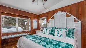 A bedroom with a wooden paneled wall, a large bed with a patterned bedspread, a bench at the window, and a white headboard. - 🌴 Charming 2BR WATERFRONT Cottage - Perfect for a Coastal Getaway! (Indian Rocks Beach)