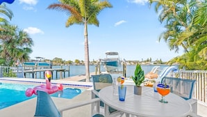 A poolside area with a table, chairs, and a flamingo float. - Water Lover's Paradise | Waterfront • Private Dock • Heated Pool (Indian Rocks Beach)