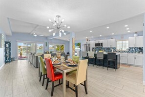 A modern kitchen with white cabinets, a central island, and a dining area with colorful chairs.